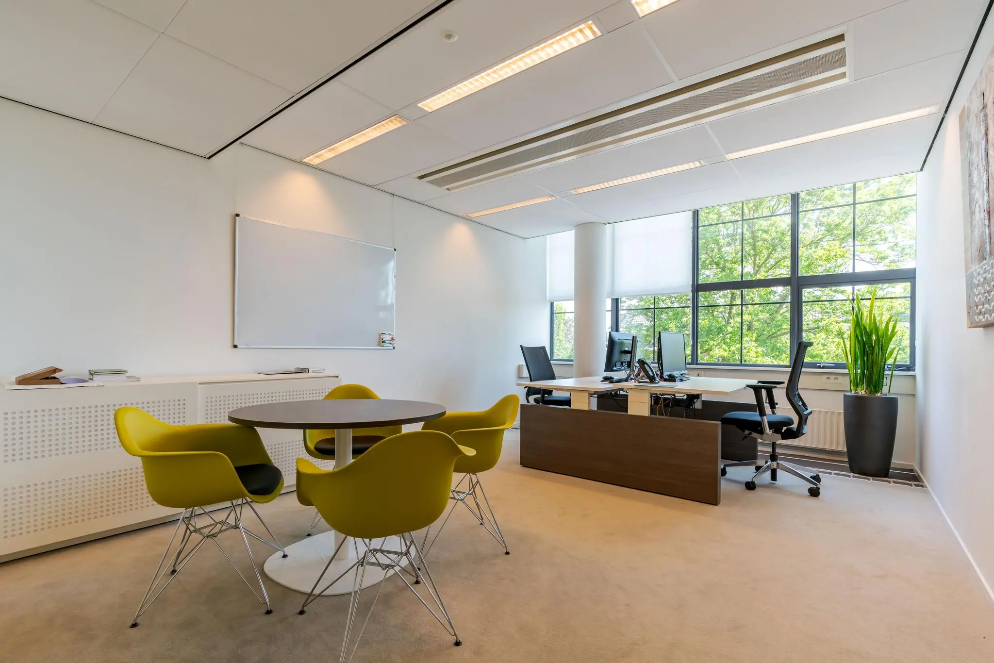 Modern kantoor aan de Van Alkemadelaan met werkplekken, vergadertafel en grote ramen met uitzicht op groen.